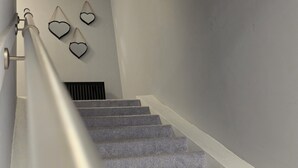 A staircase with grey carpeted steps and white handrails, leading to a landing with a black radiator.