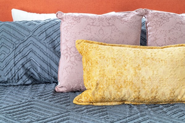 Una cama con tres almohadas de distintos diseños y colores.