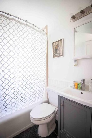 A bathroom with a shower curtain, toilet, sink, and cabinet.