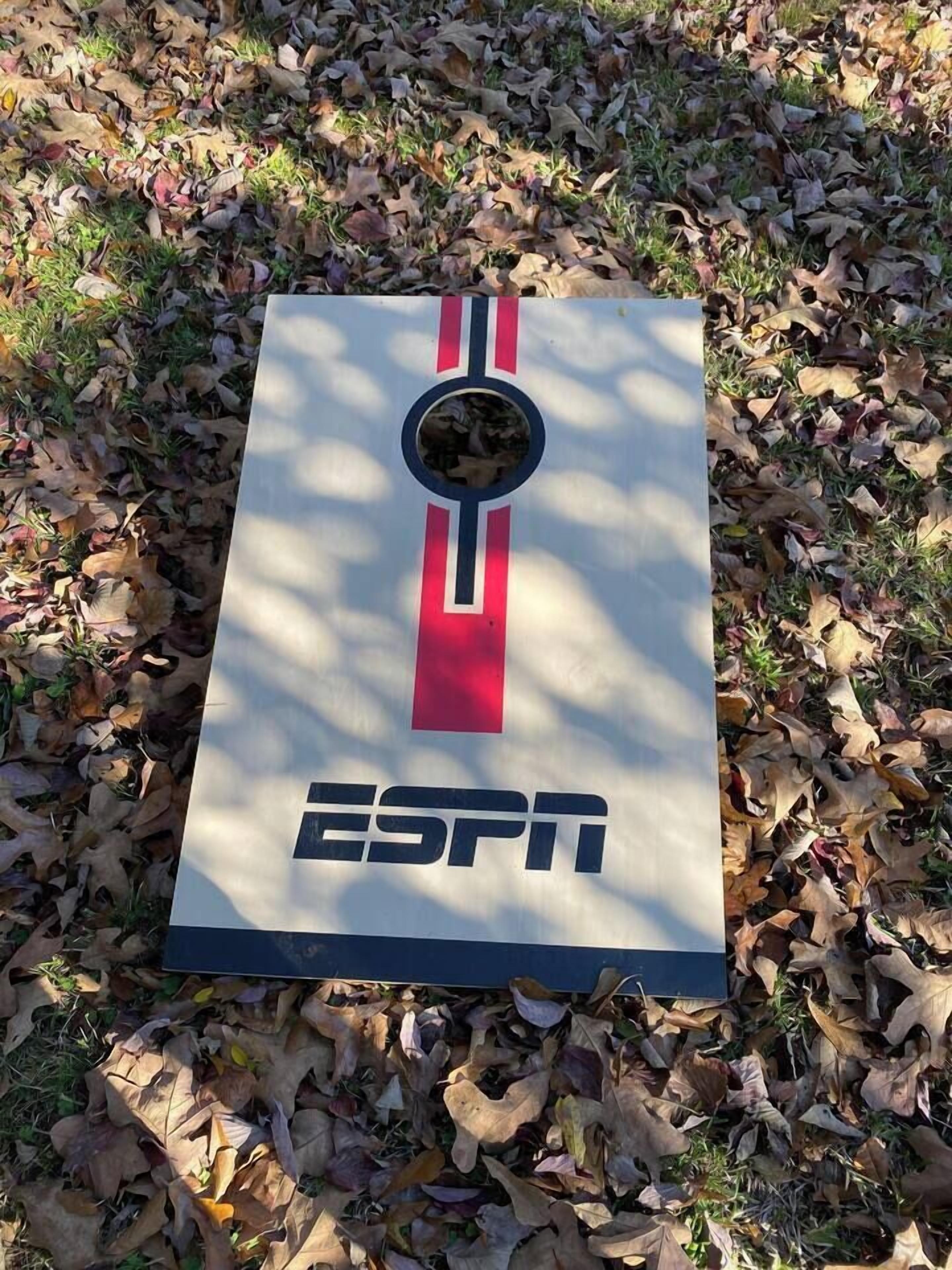 Une affiche ornée du logo d’ESPN, placée dans un espace verdoyant recouvert de feuilles mortes.