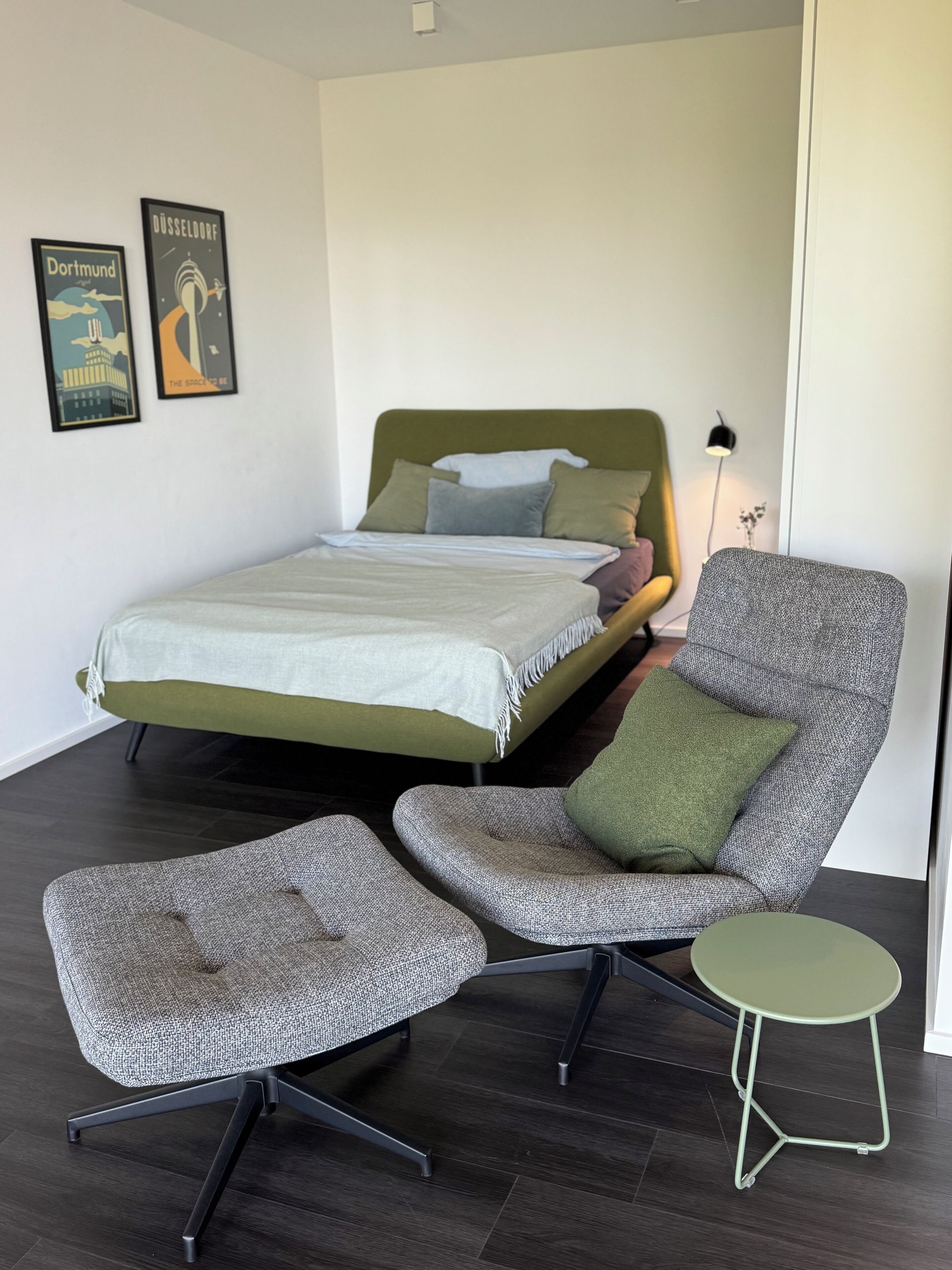 Un dormitorio con una cama, dos sillas, una mesita y dos carteles en la pared.
