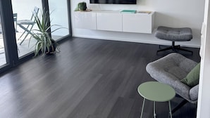 A modern living room with a flat-screen TV mounted on the wall, a grey upholstered armchair, a small round table, and a potted plant. - Chic apartment in a central location with a large balcony and views over the city (Attendorn)