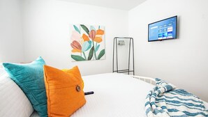 Una habitación de hotel con una cama, un televisor montado en la pared y un cuadro de flores.