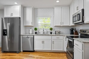 Una cocina moderna con armarios blancos, electrodomésticos de acero inoxidable, horno empotrado y una ventana con persianas.