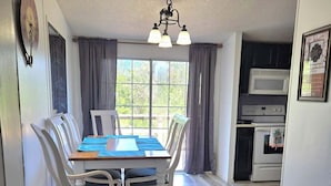 A dining area with a wooden table and chairs, a chandelier, and a view of the outdoors through large windows. - Affordable Pollyanna Ridge, By Norris Lake & Dam St Pk & ATV trails. 3BR 2Bath (Rocky Top)
