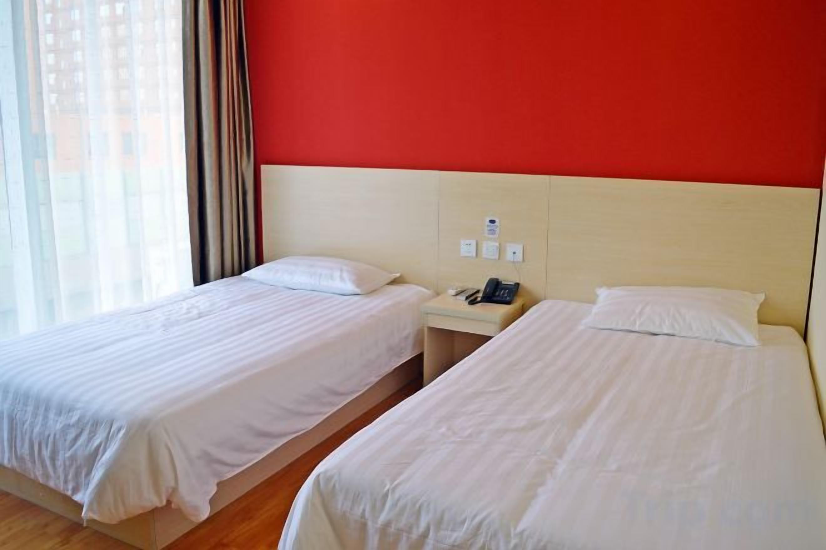 A hotel room with two beds, a nightstand, and a red wall.