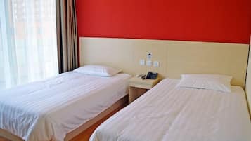 A hotel room with two beds, a nightstand, and a red wall.