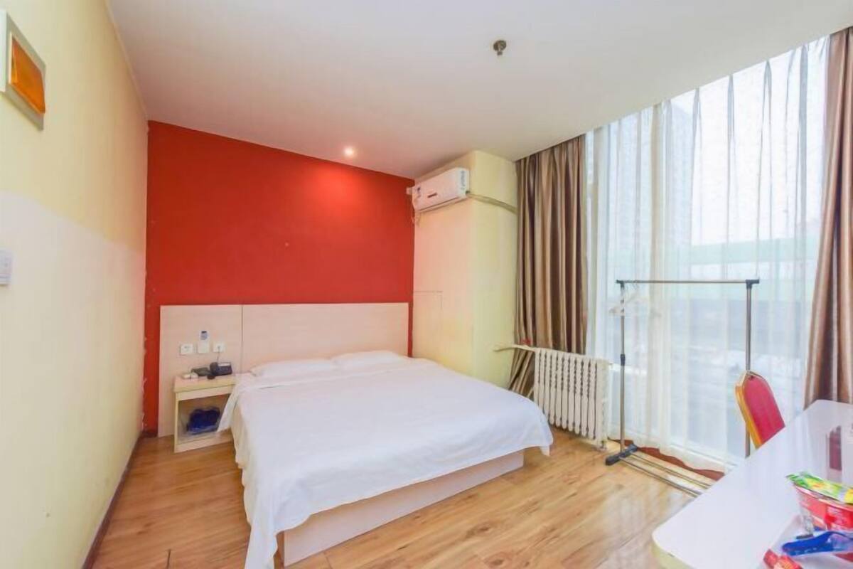 A bedroom with a bed, a radiator, a window with curtains, and a white wall.