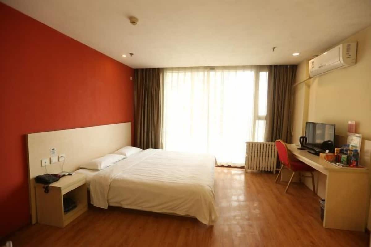 A hotel room with a bed, a desk with a computer, a chair, and a window with curtains.