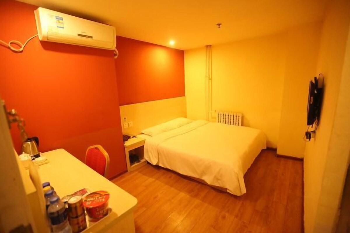 A hotel room with a bed, bedside table, and an air conditioning unit.