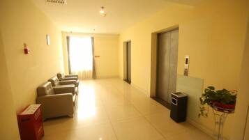 A hotel corridor with a seating area, a trash bin, a plant, and a door leading to another room.