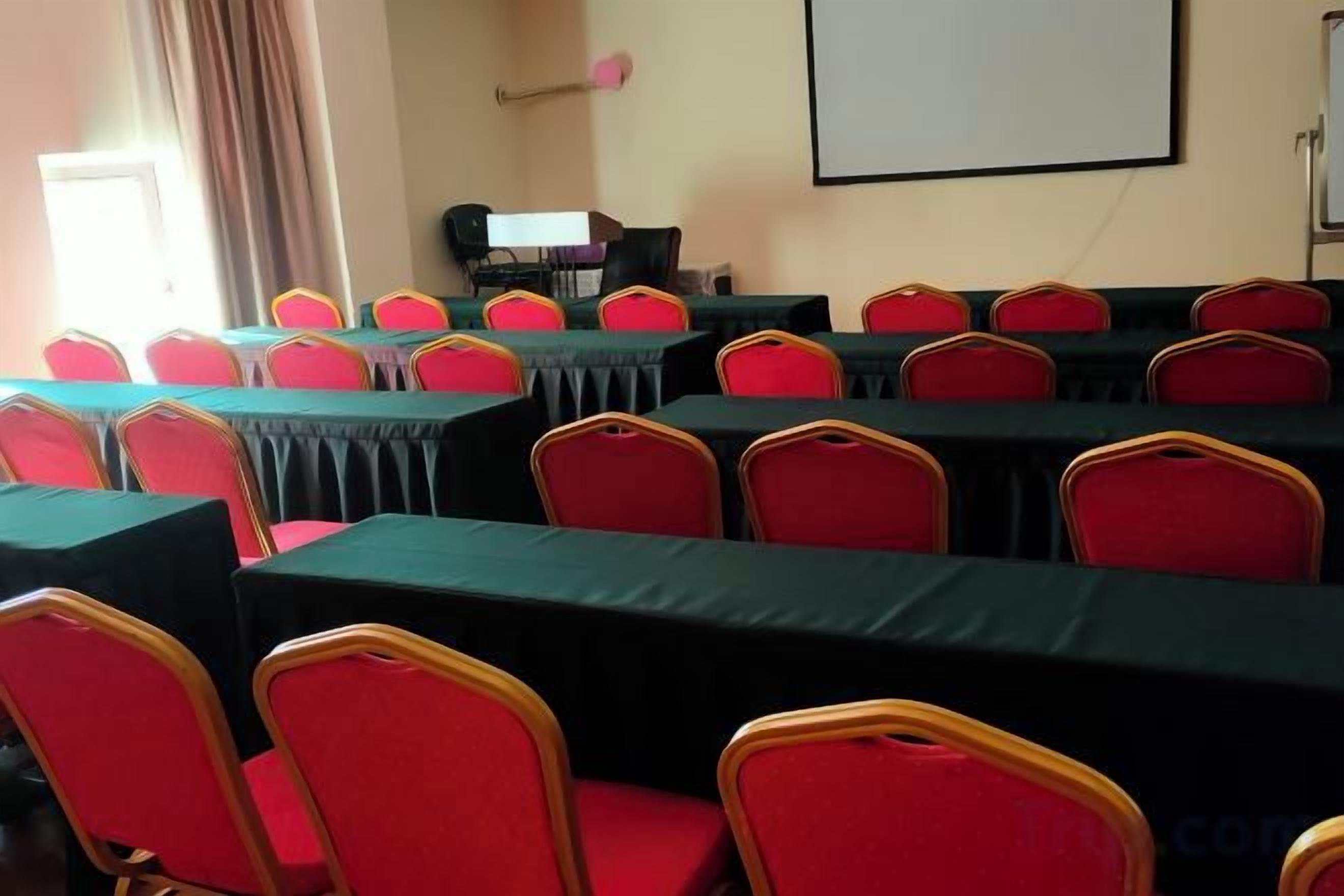 A conference room with multiple tables and chairs, a projector screen, and a window with curtains.