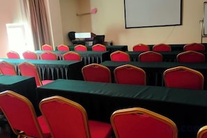 A conference room with multiple tables and chairs, a projector screen, and a window with curtains. - Henghui Binle Hotel (Shijiazhuang Zhonghua North Street Branch) (Shijiazhuang)