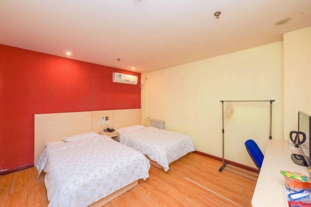 A room with two beds, a desk with a computer, and a radiator.