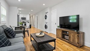 Ein modernes Wohnzimmer mit einer Couch, Couchtisch, Fernseher und einem Essbereich mit Stühlen und Tisch.