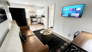 Una sala de estar moderna con un sofá de cuero marrón, una mesita de centro redonda y un televisor en la pared que muestra varios servicios de streaming.