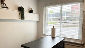 A minimalist dining area with a black table and benches, a white shelf with decorative items, and a window with blinds.