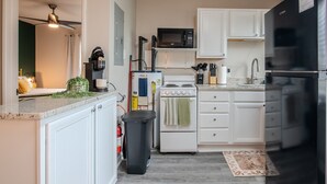 Eine kompakte Küche mit weißen Schränken, einem schwarzen Kühlschrank, einer Mikrowelle, einem Herd und einer Kaffeemaschine.