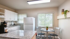 Una cocina moderna con armarios blancos, encimera de granito, refrigerador empotrado y una zona de comedor con mesa redonda y sillas.