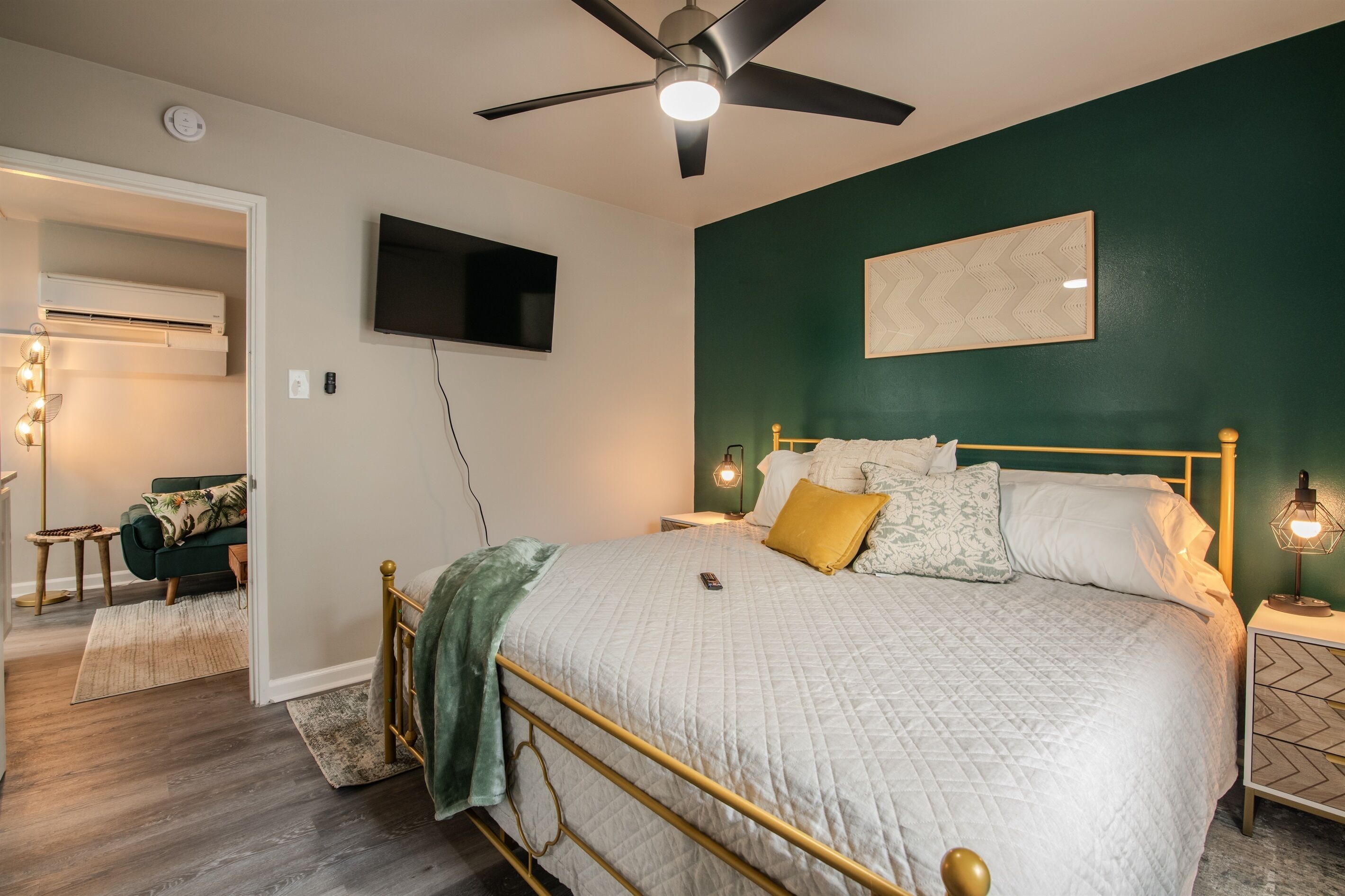 Une chambre avec un lit, un ventilateur de plafond, un téléviseur fixé au mur et un mur d’accent de couleur verte.