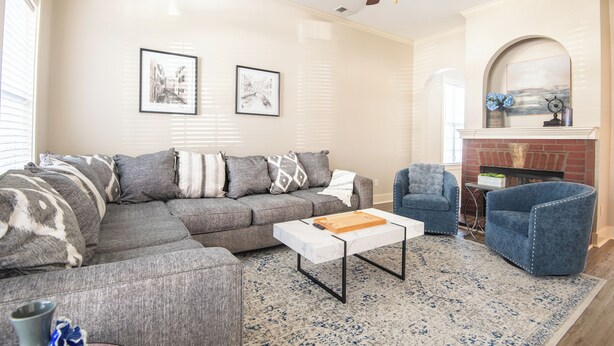 Un salon avec un canapé d’angle gris, un fauteuil bleu, une table basse blanche et une cheminée.