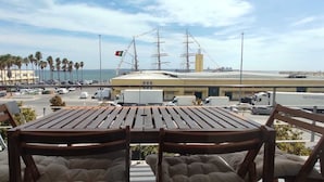 A balcony with a table and chairs overlooking a marina with yachts and a Ferris wheel.