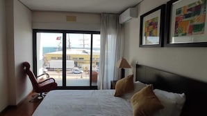 A hotel room with a large bed, a chair, a desk, and a view of the outside through a sliding door.