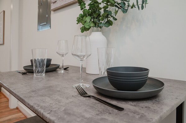 Una mesa de comedor con un jarrón blanco, vasos transparentes y cuencos apilados.