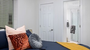 A bedroom with a bed, pillows, a remote control, and a bathroom door.