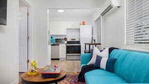 A modern living room with a teal sofa, a wooden coffee table with a children's toy, and a kitchen in the background.