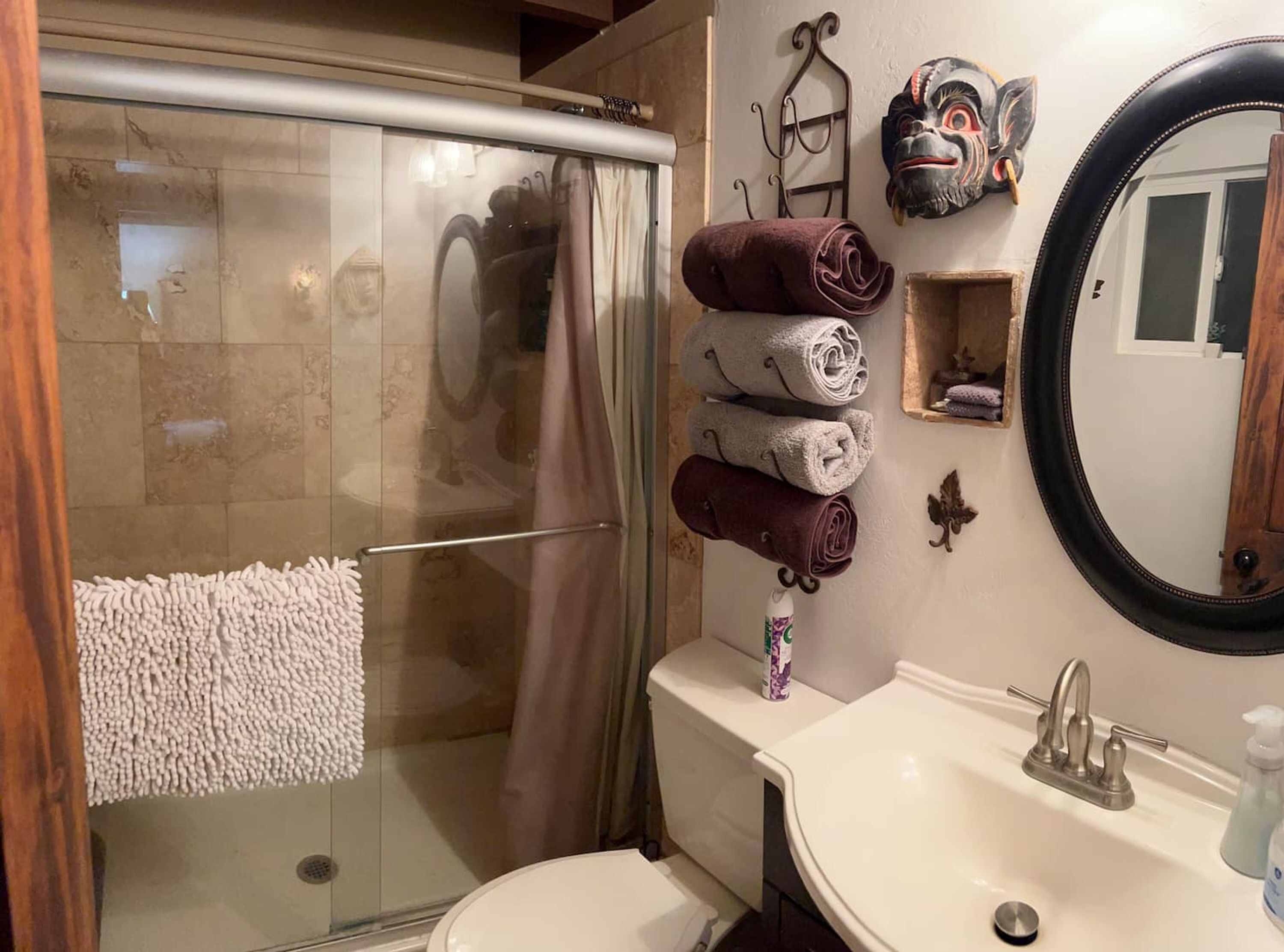 A bathroom with a glass shower enclosure, a white sink with a mirror, and a towel rack with rolled towels.