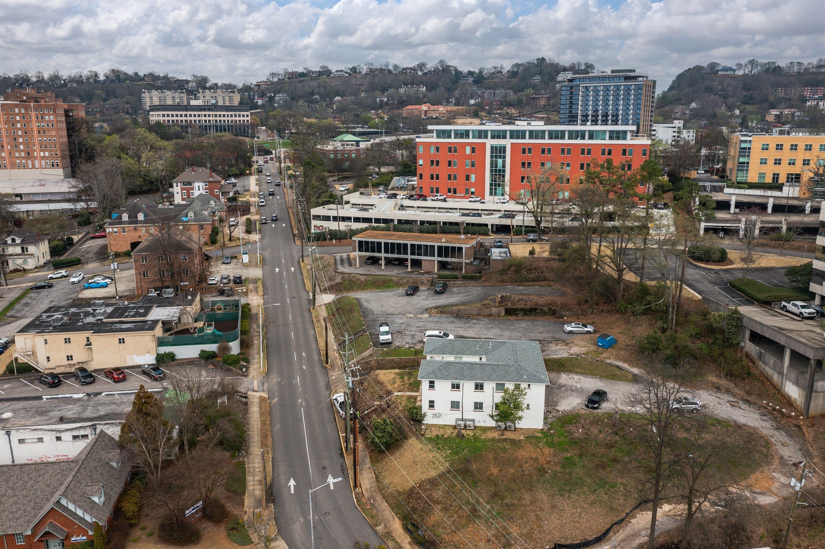 An aerial view of a cityscape with a prominent red building, a white building with a green roof, and various other structures.