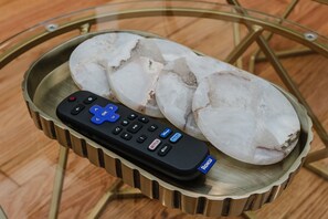 A remote control and a dish with ice cubes on a glass table.