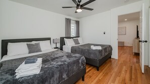 A modern hotel room with two beds, a ceiling fan, and a wooden floor.