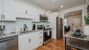A modern kitchen with white cabinets, stainless steel appliances, and a wooden floor.
