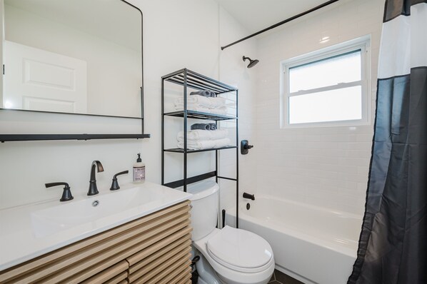 A modern bathroom with a white sink, a toilet, a bathtub, and a towel rack.