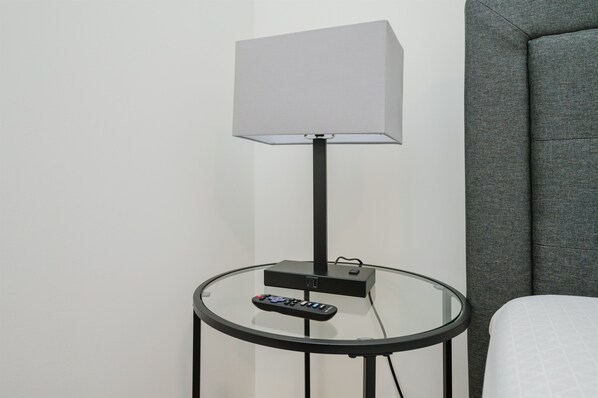 Une chambre moderne avec une table en verre, une télécommande et une lampe.