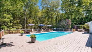 A wooden deck with a swimming pool, lounge chairs, and umbrellas.
