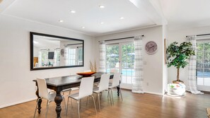 A dining area with a wooden table, white chairs, a large mirror, and a view of the outdoors.