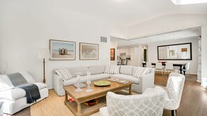 Un salon moderne avec un canapé, une table basse et des fauteuils, une cuisine en arrière-plan et un coin repas.