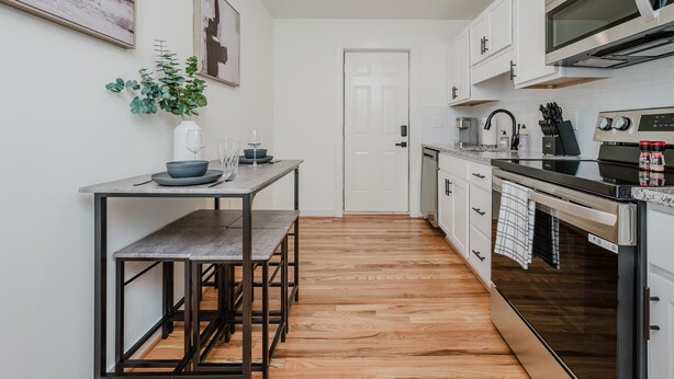 A modern kitchen with white cabinets, a stainless steel oven, and a wooden floor.