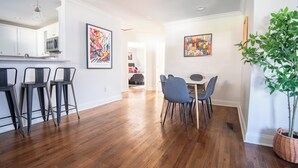 A modern kitchen with a bar area, wooden flooring, and two dining tables with chairs. - Crestwood Bloom – 3BR Getaway w/ Patio & Backyard (birmingham)