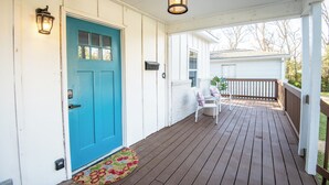 A porch with a blue door, a white railing, and a small seating area with two chairs and a table. - Crestwood Bloom – 3BR Getaway w/ Patio & Backyard (birmingham)