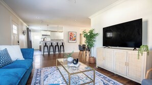 A modern living room with a blue sofa, a glass coffee table, and a TV on a cabinet. - Crestwood Bloom – 3BR Getaway w/ Patio & Backyard (birmingham)