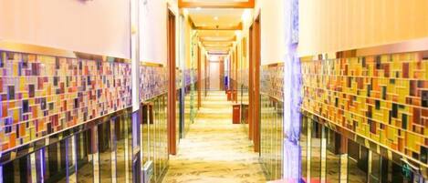 A hotel corridor with a patterned floor, glass railings, and a series of doors on one side.