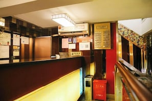 Un espace d'accueil comprenant un comptoir, un climatiseur fixé au mur et un escalier avec une rampe aux couleurs vives.