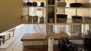 A kitchen with wooden shelves, a central island, and a view of the dining area. - North Sea vacation home Huus Eiderente - relaxation, wellness, fireplace, fiber optic WLAN (Wesselburenerkoog)