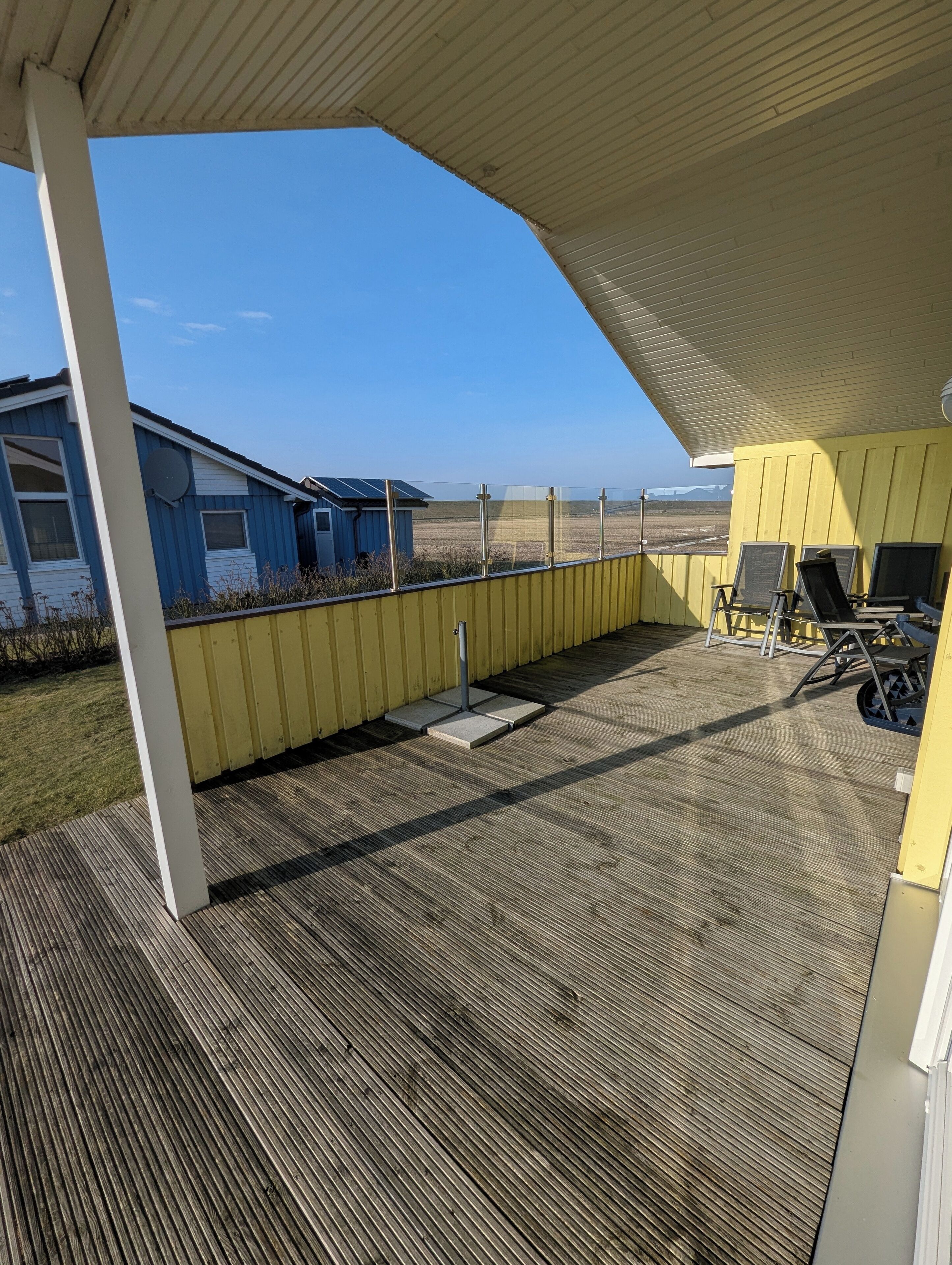 A covered patio with a view of a blue building and a yellow structure.
