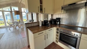 A modern kitchen with white cabinets, a stainless steel range hood, a built-in oven, and a coffee maker. - North Sea vacation home Huus Eiderente - relaxation, wellness, fireplace, fiber optic WLAN (Wesselburenerkoog)