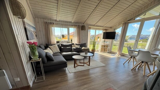 A modern living room with a sectional sofa, a round coffee table, and a dining area with a table and chairs. - North Sea vacation home Huus Eiderente - relaxation, wellness, fireplace, fiber optic WLAN (Wesselburenerkoog)